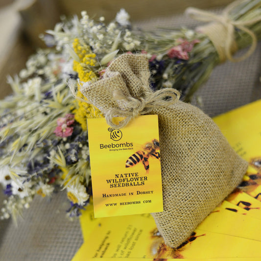 Bumblebee flower ball made of clay and wildflower seeds.  In a hessian bag with flowers behind. 